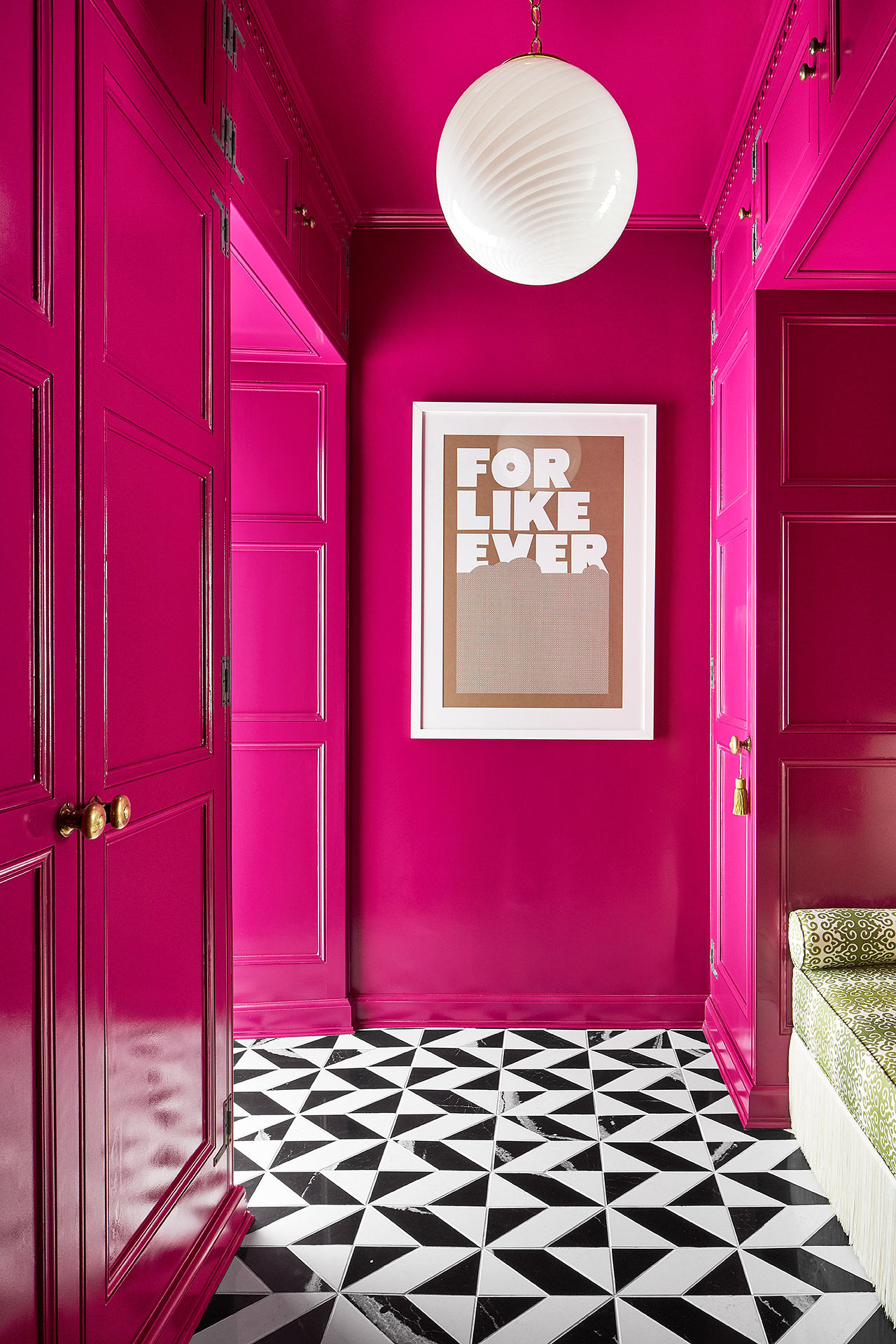 An entryway with hot pink walls, black and white quartz tiled flooring, and a gorgeous light fixture.